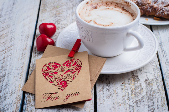 Valentine's day concept with two hearts, gift card and cup of coffee, almond croissant on wooden table background. Top view,copy space. Romantic holiday