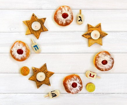 Wooden candlesticks in the shape of star, donuts, golden chocolate coins and dreidels on background of white painted wooden planks with space for text. Jewish holiday Hanukkah. Top view, flat lay.