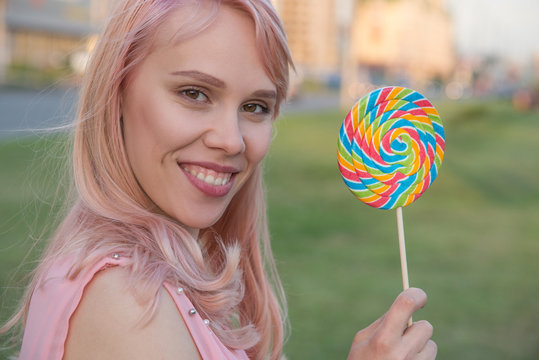 Beautiful young girl holds caramel candy in the form of a multi-colored spiral on the street in summer