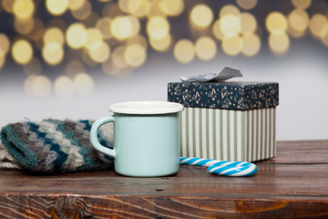 vintage bright green cup with hot tea and warm gloves on wooden table and holiday lights