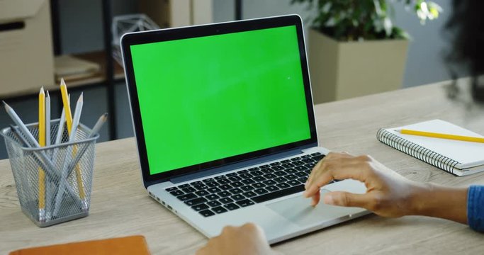 Over shoulder view on male hands working on the laptop computer which is on the white wooden table in the office. Green screen. Chroma key. Close up