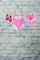 Children's pink body, bib and red shoes, dry on a rope against a white brick wall.