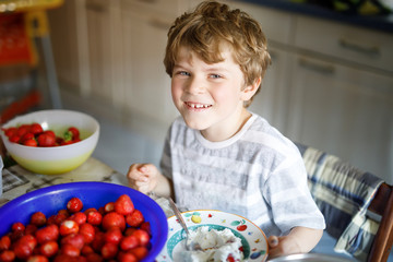 Little blond kid boy helping and making strawberry jam in summer
