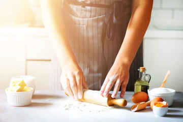 Female hands kneading dough, baking background. Cooking ingredients - eggs, flour, sugar, butter, milk, rolling pin on white style kitchen. Copy space