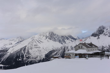 Panorama of French Alps with mountain ranges covered in snow and clouds and with mountain hut in winter