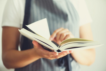 Girl wearing grey apron and reading book. Lifestyle concept