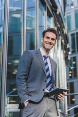 Fototapeta premium businessman stands in front of an office building with a tablet