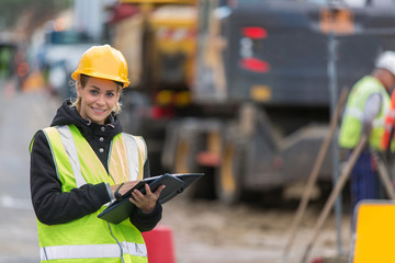 female builder in hardhat with tablet pac at construction with her team