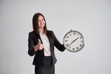 business woman shows on the big round clock , on a gray wall background in the office