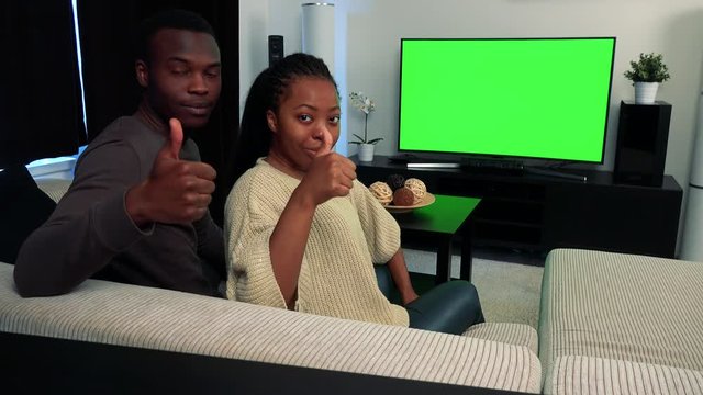Young black couple watch television in living room and then show thumb up 