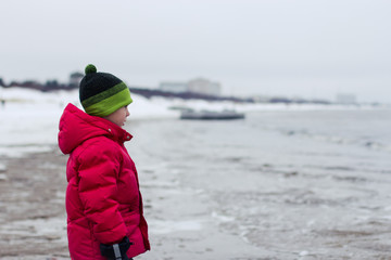 a child looks at the sea in winter, stands sideways, thoughtful