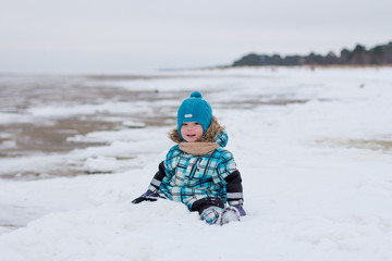 kid playing in the snow outdoors. looks straight and smiling