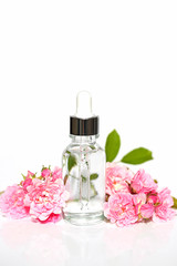 Obraz na płótnie Canvas Cosmetics with rose extract. Serum for face skin with rose extract in a transparent glass bottle with a pipette and pink roses on a white background.Botanical natural cosmetics concept 