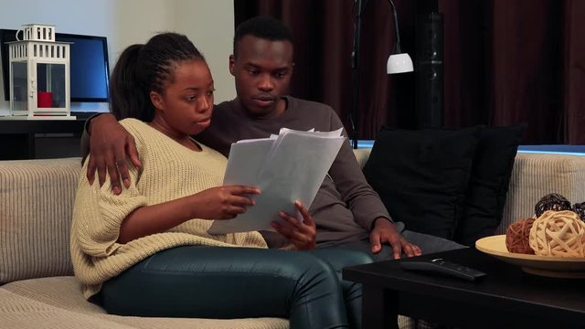 Young black couple read some documents and talk about it in living room 