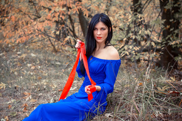 Modern Snow White in blue dress holds an apple in the woods. Snow White princess with the famous red apple. Girl holds a ripe Apple sitting in forest