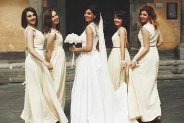 Bride and bridesmaids in yellow dresses look over their shoulders posing on the street somewhere in Italy