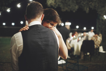 Groom hugs bride tender while they dance on the backyard in the evening