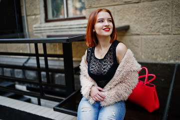 Red haired girl with red handbag posed at street of city.