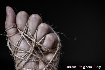 Woman hand tied with wire on dark background in low key. International human rights day concept.