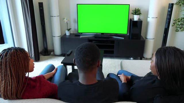 Three african friends watch television in living room and talk about something 