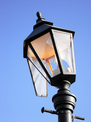 Streetlight burning during the day as a symbol of waste, losses and vandalism. Broken hooligans street lamp.
