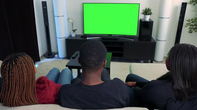 Three african friends watch television and then they talk to camera 