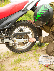 Man adjusting bolts with socket wrench on rear motorcycle wheel.