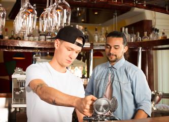 Young trainee bartender pouring beer under supervision from manager.