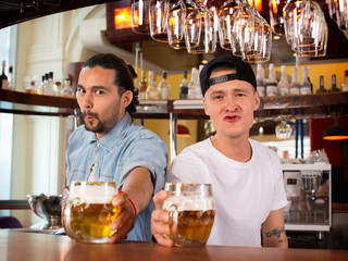 Two bartenders making funny humorous faces and offering beer.