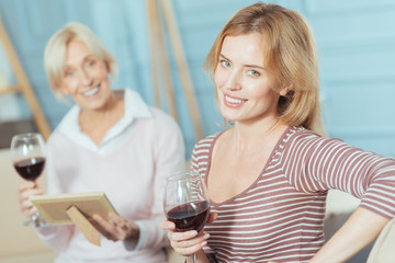 Drinking together. Positive friendly relatives of different age having a good time together while sitting on a soft sofa and drinking tasty red wine from beautiful glasses