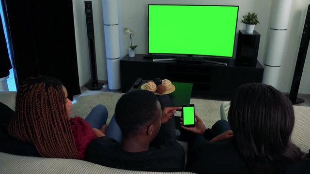 Three african friends television in living room and they work together on phone