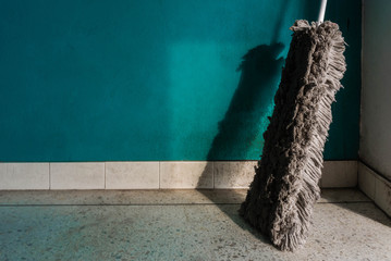 Old mop leaning against the wall in shades of green and have plenty of sunshine,.A dirty mop or swab on the old wall background