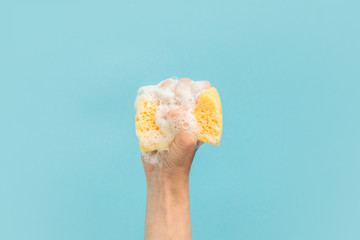 cropped view of hand holding washing sponge with foam, isolated on blue - obrazy, fototapety, plakaty