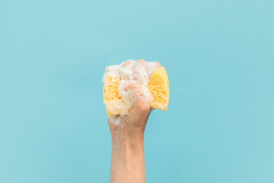 cropped view of hand holding washing sponge with foam, isolated on blue