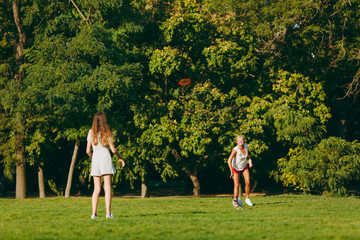 Mother and daughter throwing orange flying disk to small funny dog, which catching it on green...