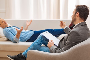 Therapy aids. Experienced professional male psychologist   sitting in the armchair and listening to...
