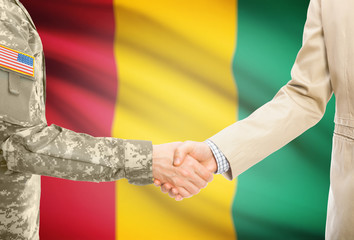 USA military man in uniform and civil man in suit shaking hands with adequate national flag on background - Guinea