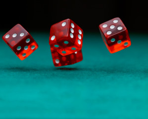 Photo of several red dice falling on green table on black background