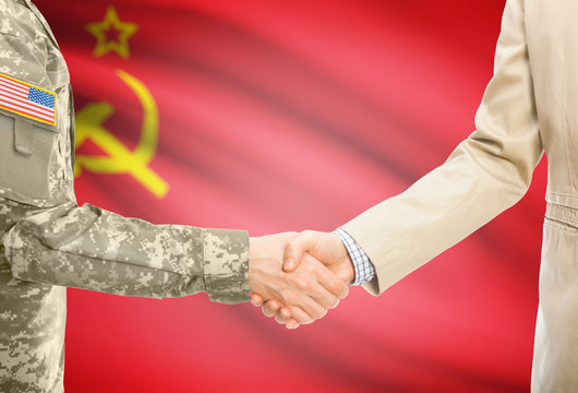 USA military man in uniform and civil man in suit shaking hands with adequate national flag on background - Soviet Union - USSR