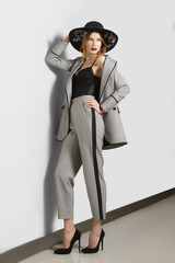 Full lenght portrait of wooman in jacket, pants with stripe and broad-brim hat with flowers