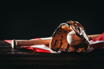 close-up view of baseball glove with ball and bat on wooden table and us flag on black