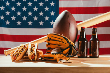 close-up view of beer with hot dogs and sport equipment with american flag behind