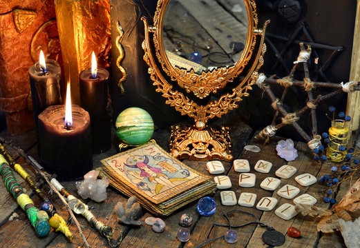Tarot cards, magic wands, runes, black candles with mirrow and old book. Occult, esoteric, divination and wicca concept. Mystic and vintage background