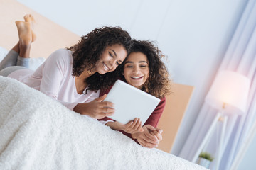 Harmony and understanding. Adorable young girls smiling cheerfully while lying on a bed and looking at a screen of their tablet computer together.