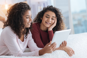Joyful time in family circle. Selective focus on a curly haired girl resting her chin on a hand while lying next to her sister and smiling during a family film session.