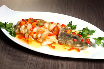 Grilled fish on white plate with herbs and lemon on wooden background, top view. Mediterranean luxurious seafood concept.
