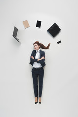 overhead view of businesswoman with various office supplies above head isolated on grey