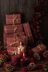 Three candles of crimson and pink color on the background of gift boxes with cones, leaves and daisies.