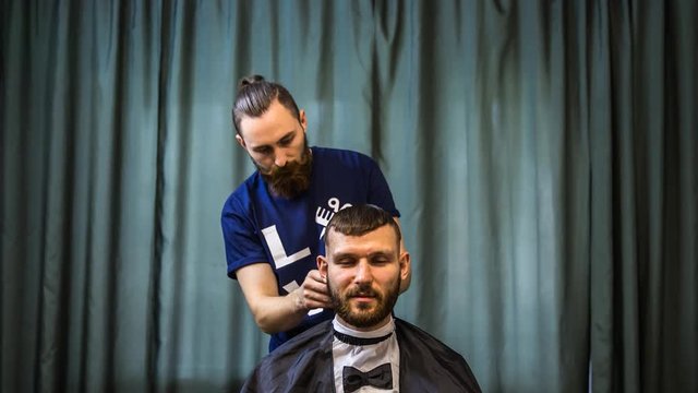 A confident man is visiting a hairstylist in a barbershop. The hairdresser is in the process of cutting the customer. Timelapse.