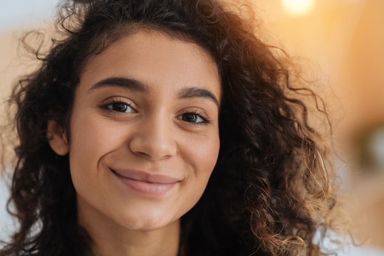 Heavenly beauty. Charming curly haired young lady looking into the camera with eyes full of happiness and smiling cheerfully indoors. - Powered by Adobe
